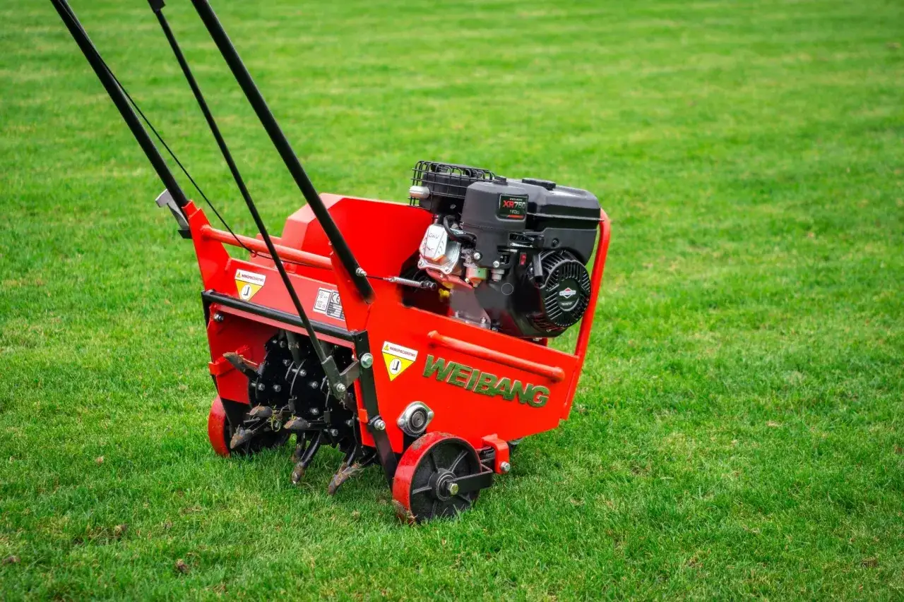 Czerwony aerator Weidemann na zielonej trawie. Zastanawiasz się, co najpierw: aeracja czy wertykulacja? Ten sprzęt pomoże Ci zadbać o trawnik.