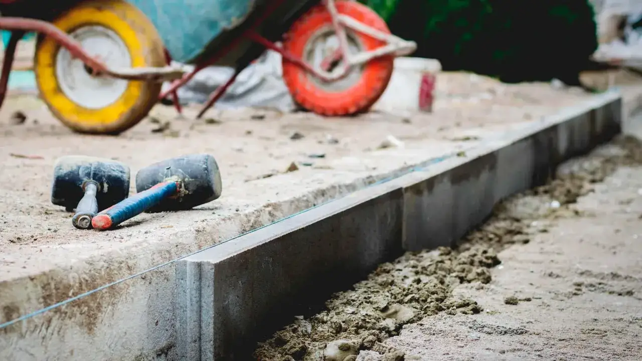 Dwa gumowe młotki leżą obok świeżo ułożonych krawężników, gotowych do docinania krawężników pod kątem. W tle widać taczkę.