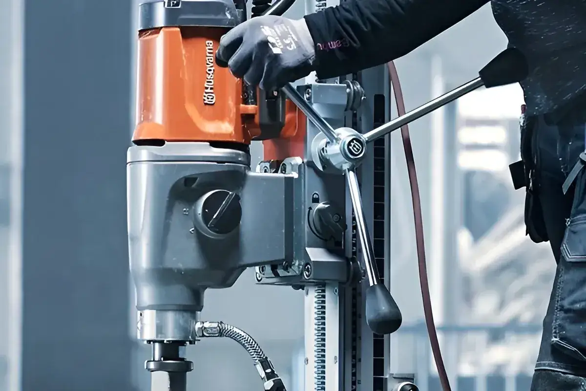 Ręka w rękawicy obsługuje wiertnicę diamentową Husqvarna, pokazując, jak wiercić w betonie zbrojonym.