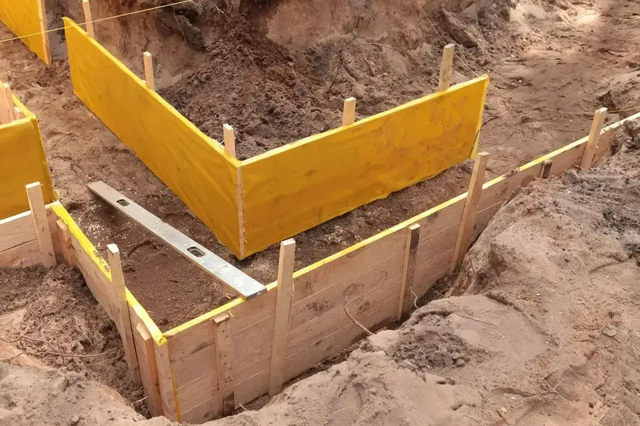 Trwa pogłębianie piwnicy. Wykopano fundamenty, które są obudowane drewnianymi deskami i żółtą folią.