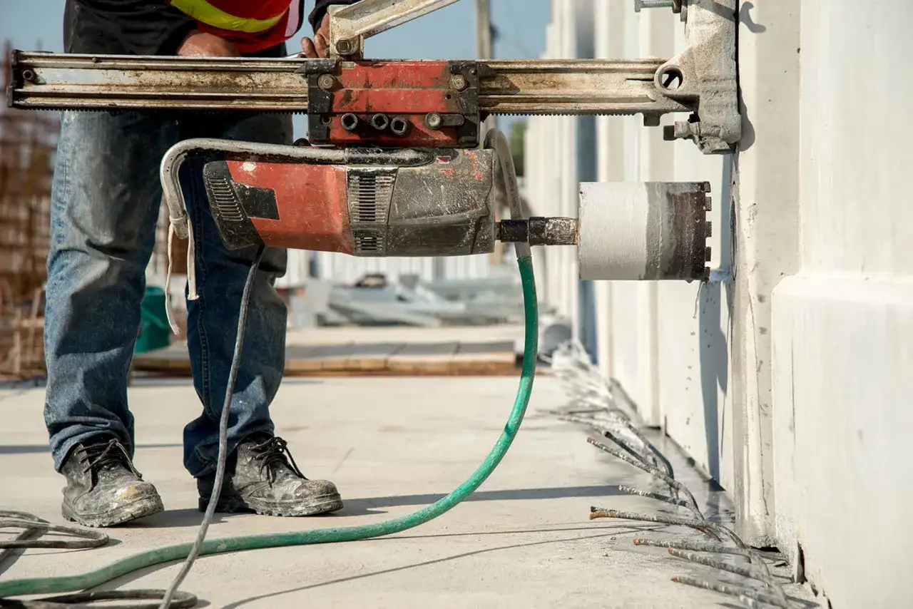 Robot wiertniczy wykonuje precyzyjne cięcie betonu. Wiertło rdzeniowe zagłębia się w ścianę, a zielony wąż dostarcza wodę chłodzącą.