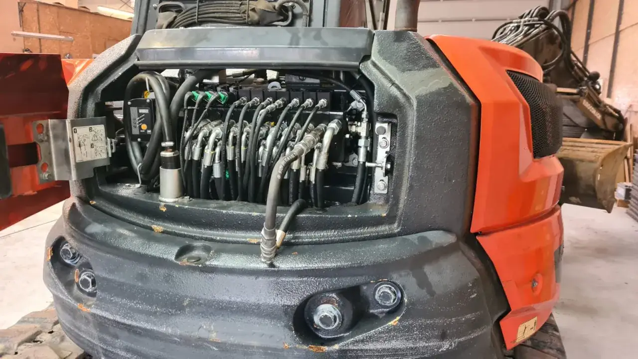 Widok wnętrza maszyny budowlanej, gdzie trwa naprawa zagęszczarek. Widoczne przewody hydrauliczne i elementy sterujące.