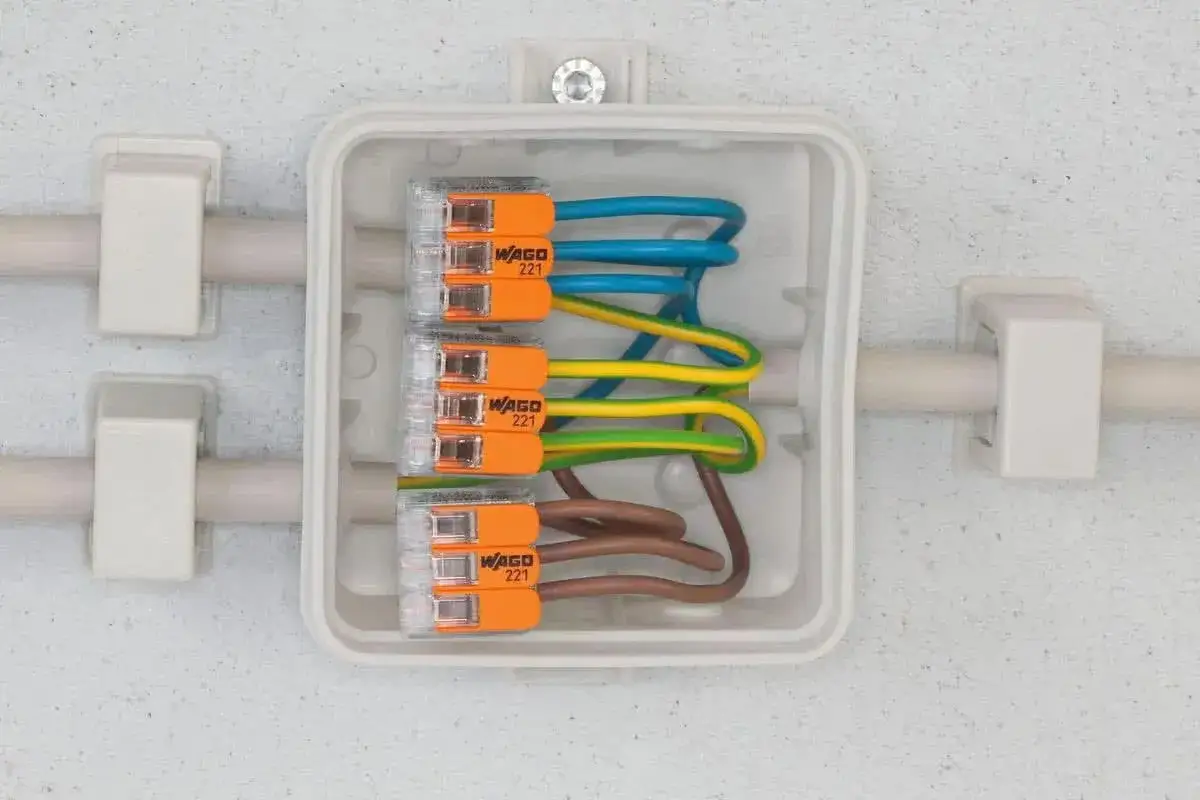 Różne rodzaje kostek elektrycznych WAGO 221 łączą przewody w białej puszce instalacyjnej.
