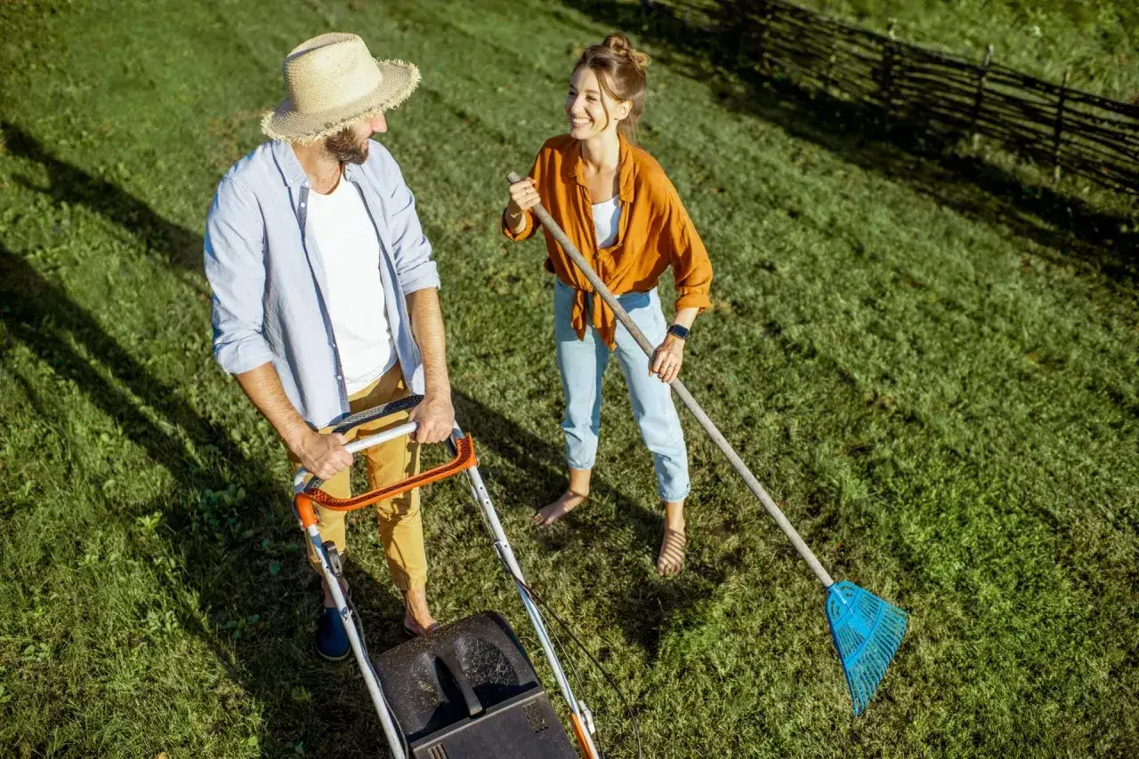 Para, kiedy rekultywacja trawnika, kosi trawę, a ona grabi. Uśmiechnięci, cieszą się pracą w ogrodzie.