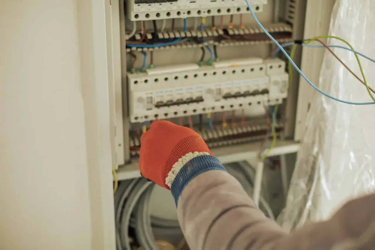Ręka w pomarańczowej rękawicy pracuje przy skrzynce elektrycznej. Instalacja zgodna z agregat prądotwórczy przepisy ppoż.