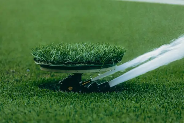 Zraszacze wynurzalne na boisku sportowym, jeden z rodzajów zraszaczy wynurzalnych, nawadnia zieloną murawę.